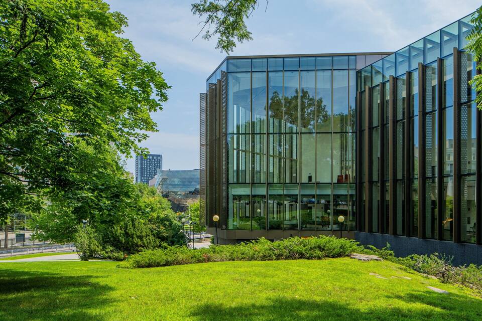 A modern glass building surrounded by lush green trees and grass.