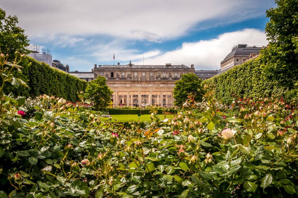 A historic building with a formal garden and blooming roses.