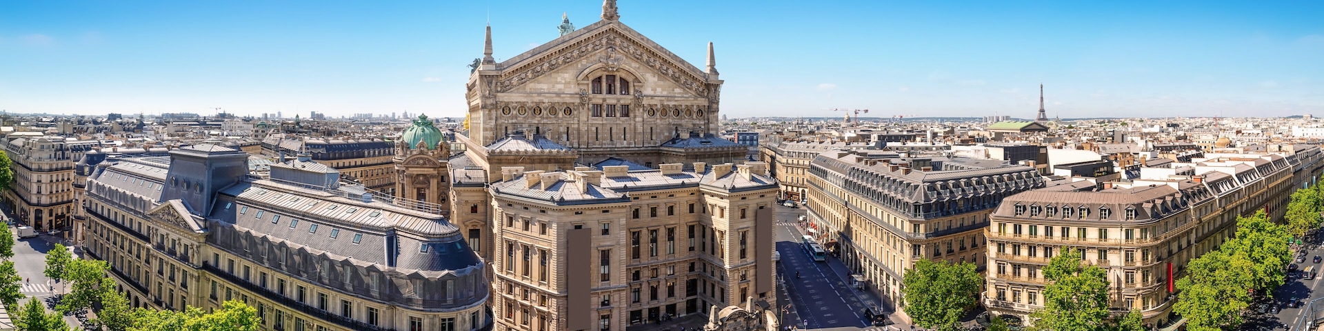 Um edifício histórico com arquitetura ornamentada, uma grande praça aberta e edifícios urbanos ao redor.