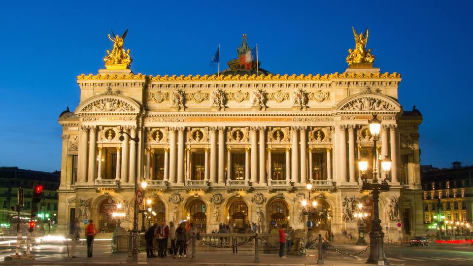 A grand historic building with ornate sculptures and columns, featuring a prominent statue on the roof.