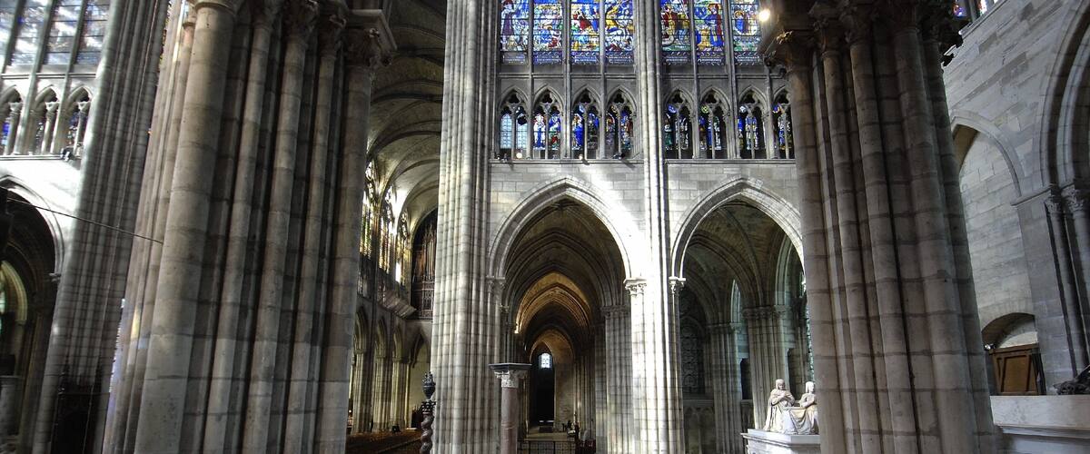 A cathedral interior with high vaulted ceilings, large stained glass windows, and classical columns.