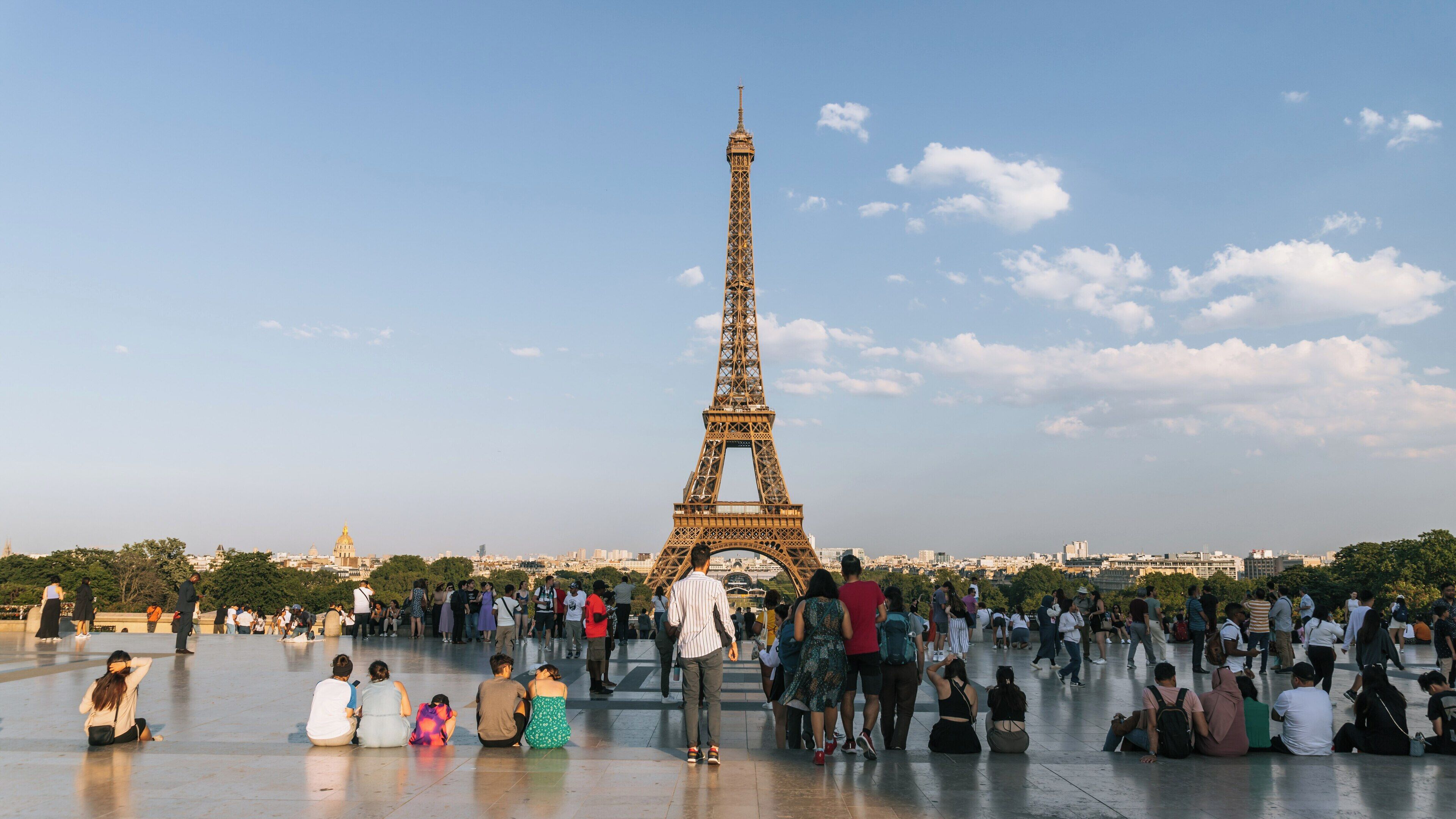 Visitors enjoy a sunny day admiring the Eiffel Tower in the 7th Arrondissement of Paris, creating lasting memories and capturing moments with friends