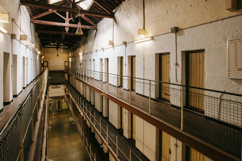 A long corridor with multiple doors and windows, metal railings, and a high ceiling with exposed beams.