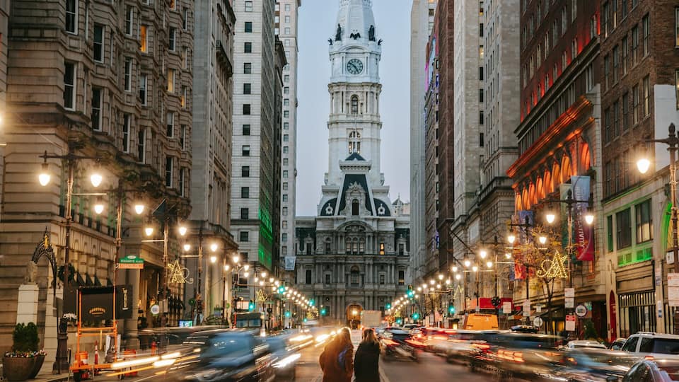 A city street with tall buildings, a clock tower, and traffic lights.