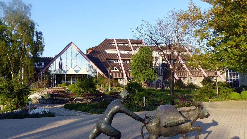 A statue of a person pulling a bull, a modern building with glass windows, and a park with trees and a pond.