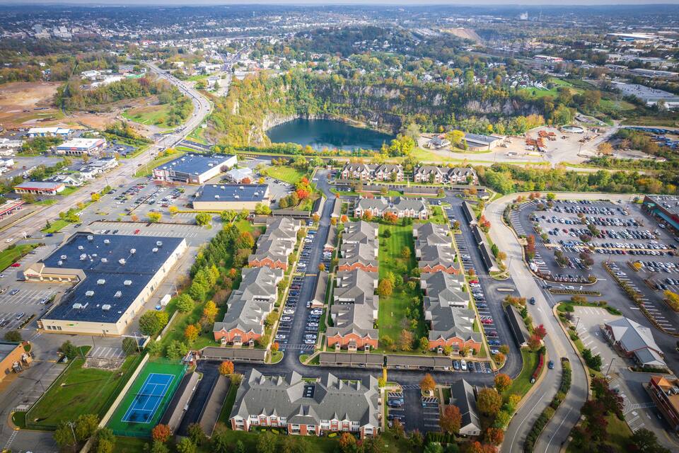 An aerial view of a suburban area with a large parking lot, a tennis court, and a lake in the background.