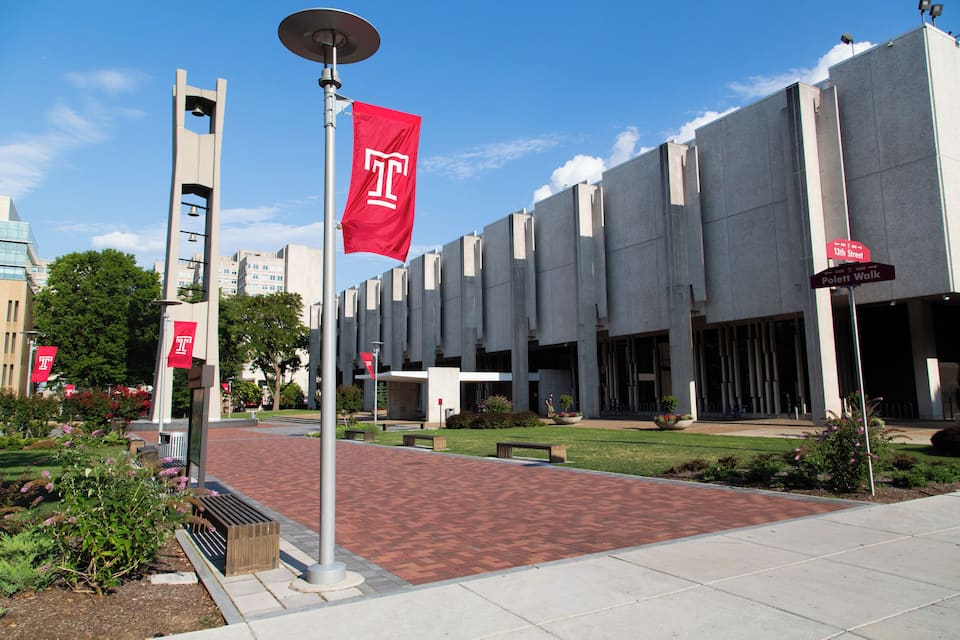 A campus with a bell tower, red flags, and a paved walkway.
