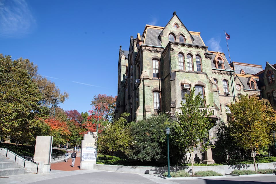 A historic building with a flag, surrounded by trees and a clear blue sky.