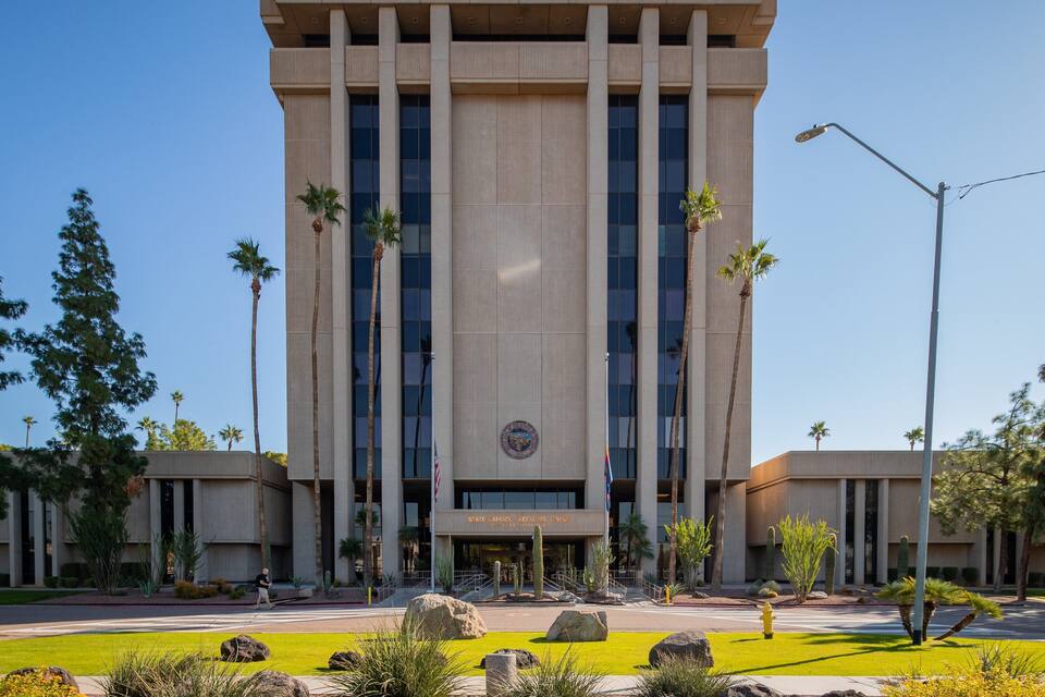 Un edificio moderno con un emblema central, rodeado de palmeras y rocas.