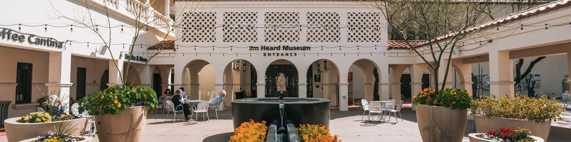 A courtyard with a fountain, potted plants, outdoor seating, and the entrance to the Heard Museum.