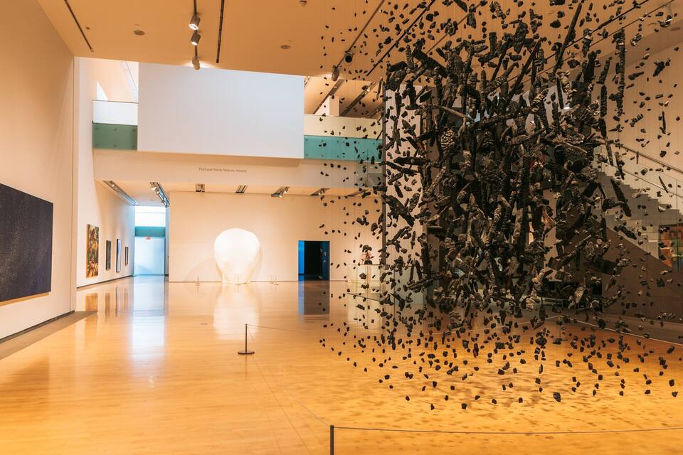 An art gallery with a large sculpture of black objects suspended from the ceiling.