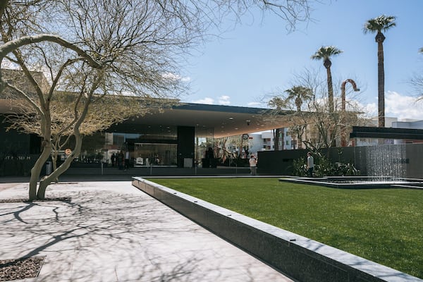 A modern building with a glass facade, palm trees, and a water feature.