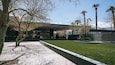 A modern building with a glass facade, palm trees, and a water feature.