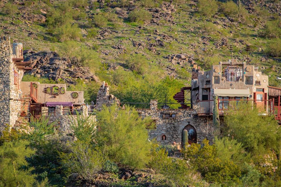 A rugged hillside with stone buildings, including a tower and a structure with a wheel.
