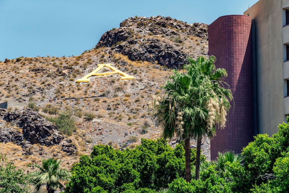 A desert landscape with a large golden triangle, a tall red building, and palm trees.