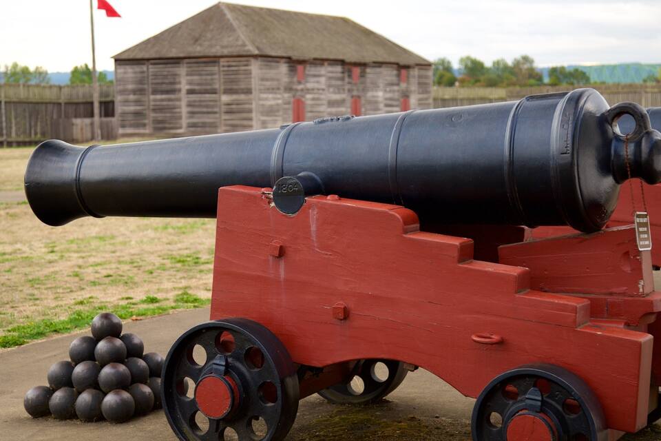 A historical cannon with a red carriage, positioned outdoors with a wooden building and a flag in the background.