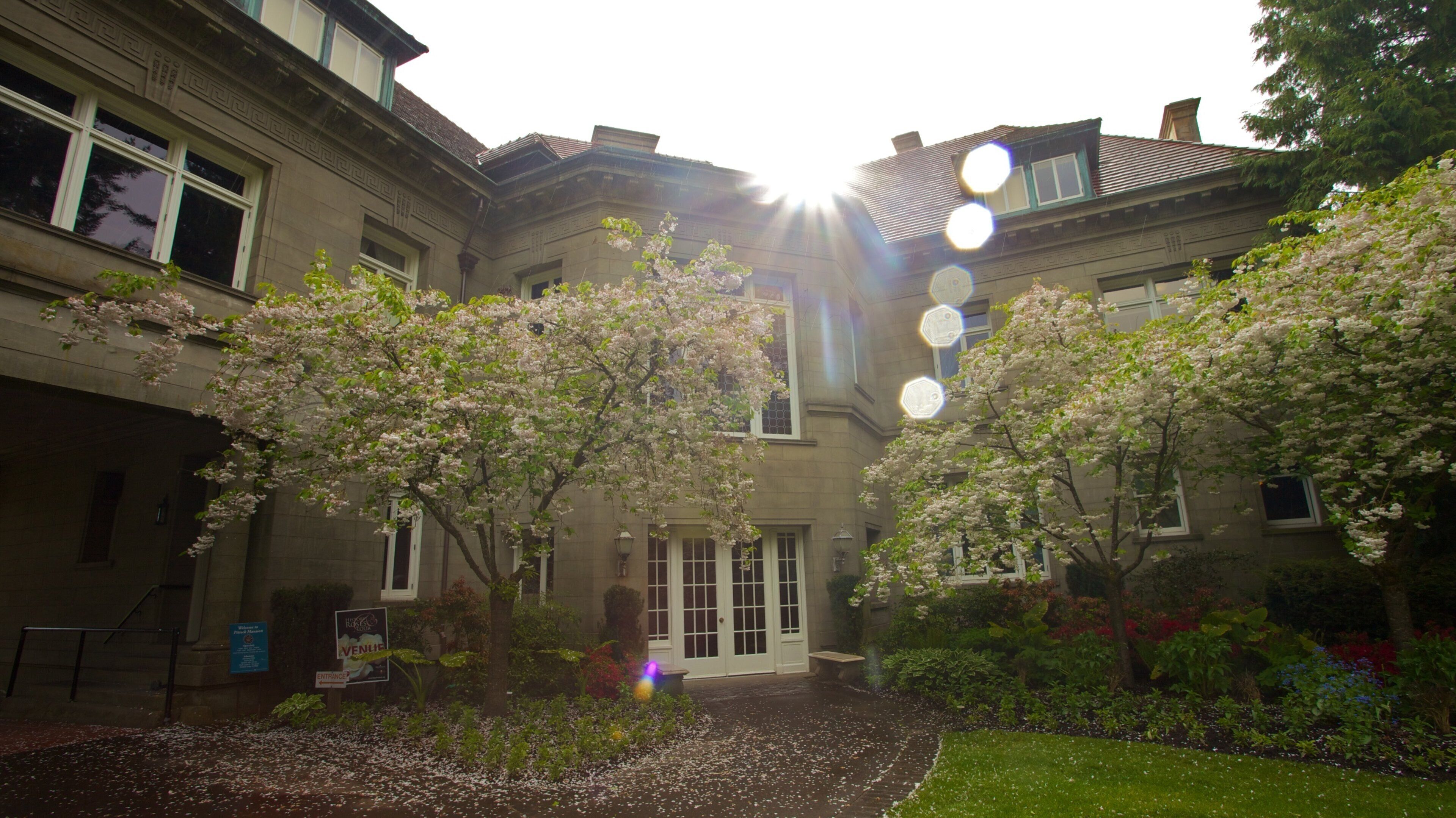 Pittock Mansion surrounded by blooming trees under a bright sun in Portland, Oregon