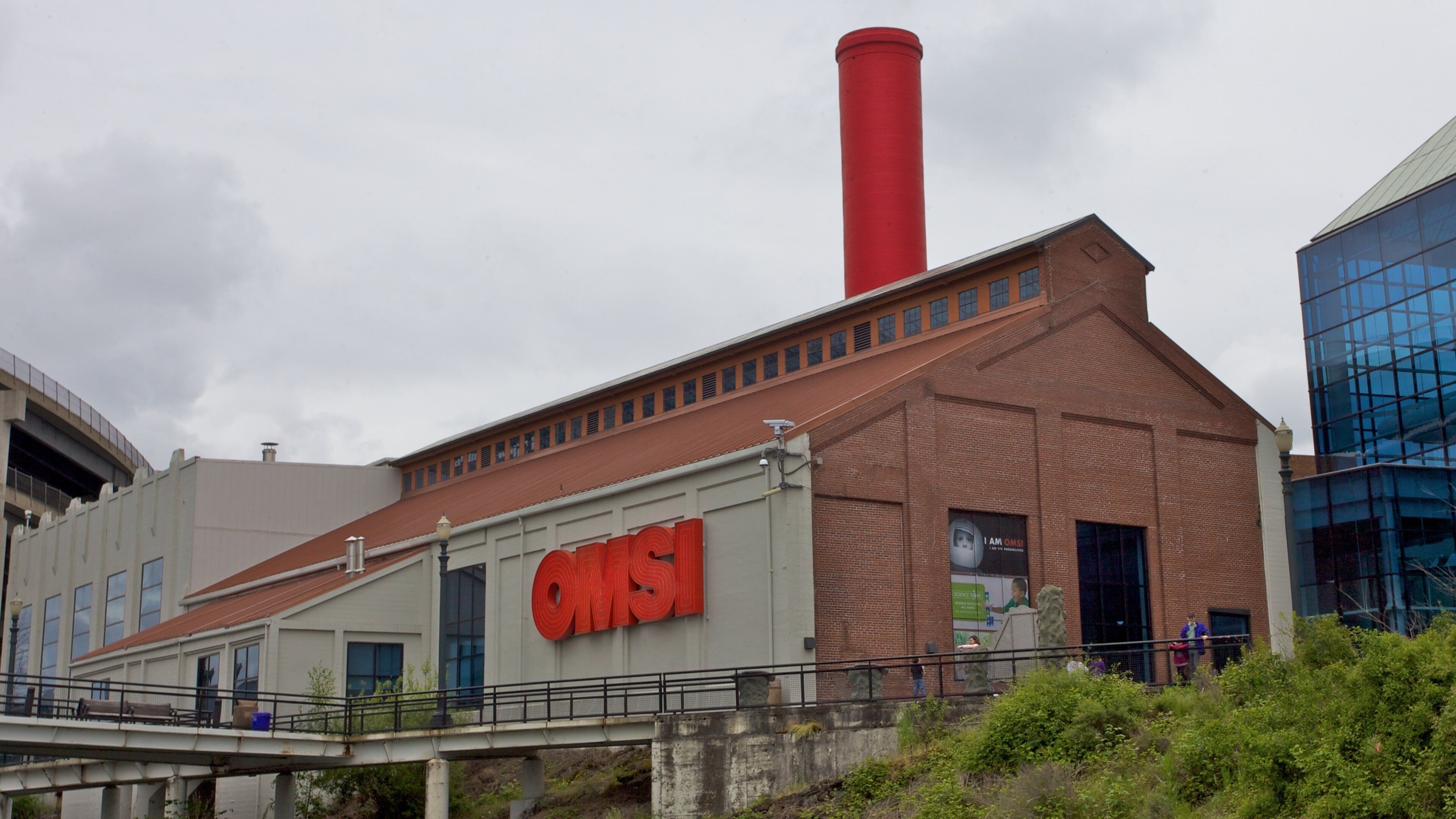 Un edificio industrial grande con una chimenea roja destacada y las letras "QMS" en su lateral.