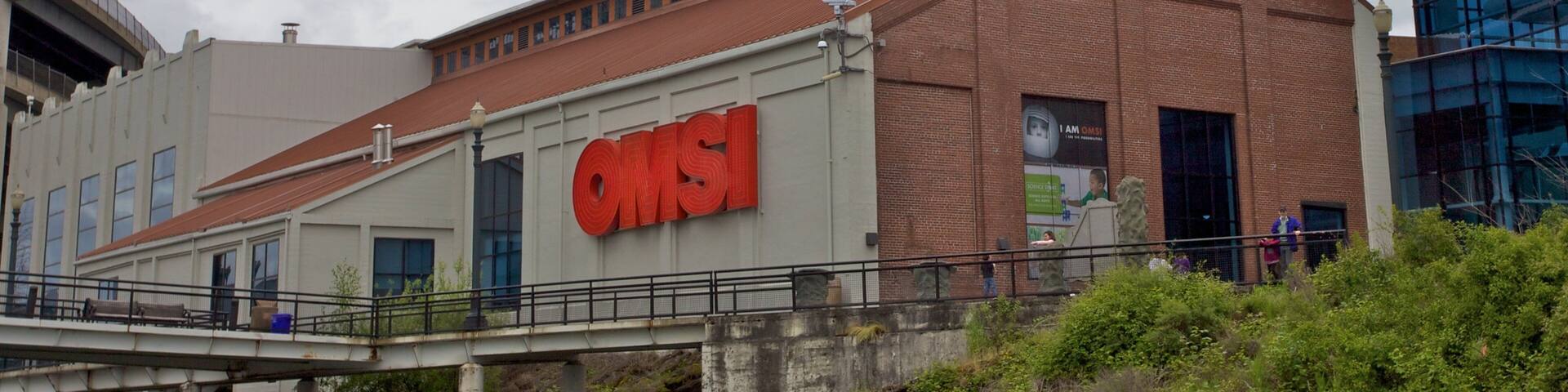 A large industrial building with a prominent red chimney and the letters "QMS" on its side.