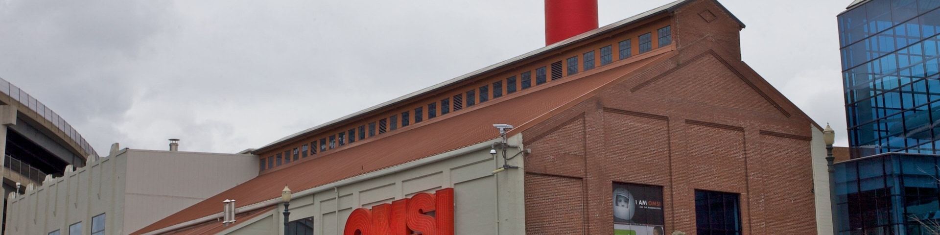 Um amplo edifício industrial com uma chaminé vermelha destacada e as letras "QMS" na lateral.