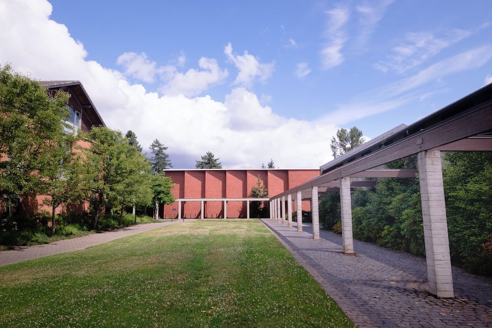 A courtyard with a brick building, a covered walkway, and surrounding greenery.