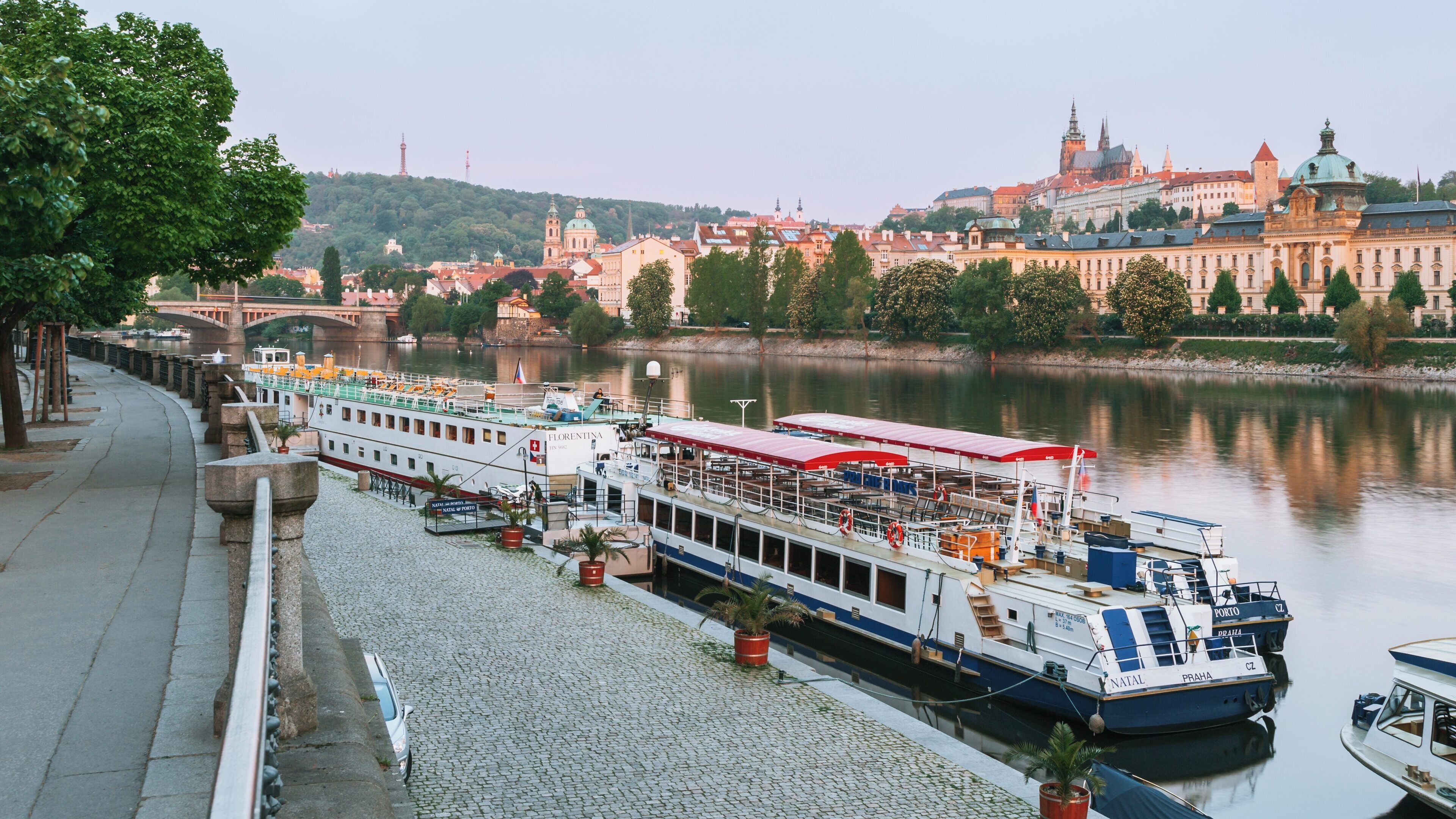 Beautiful view of Prague Castle over the Vltava River with boats docked along the riverbank in Prague, Czechia during early evening