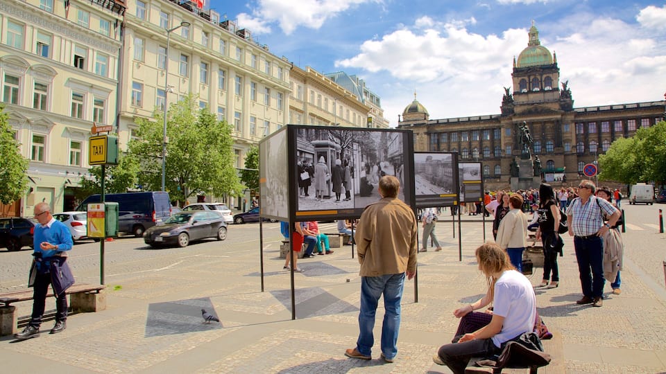 A busy city square with historical buildings, a tram, and people visiting an information board.