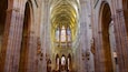 A cathedral interior with tall arched ceilings, stained glass windows, and ornate statues.