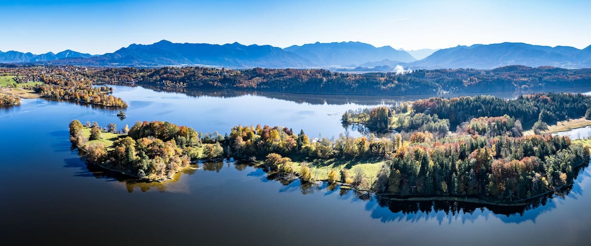A calm lake surrounded by autumn-colored trees and mountains in the background.