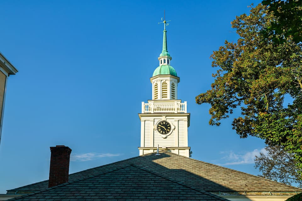 A church steeple with a clock and a weather vane.