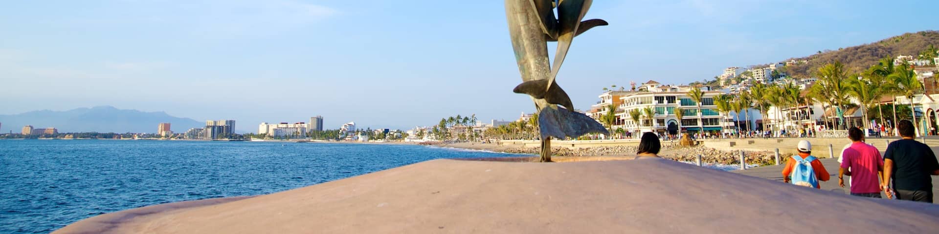 A dolphin sculpture on a beach with a cityscape in the background.