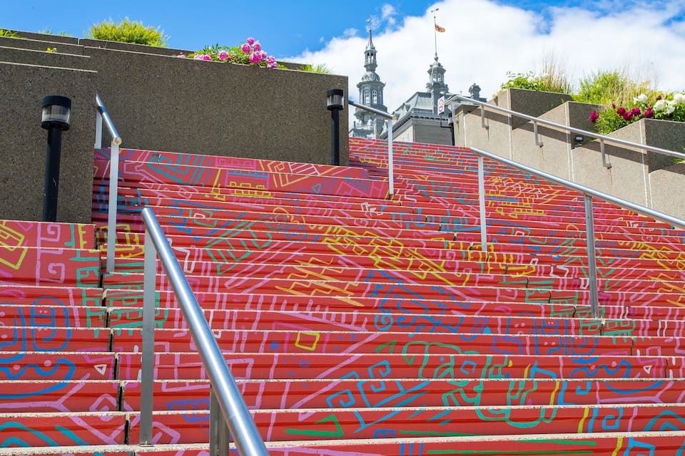 A staircase with colorful graffiti, metal railings, and a building with a clock tower in the background.