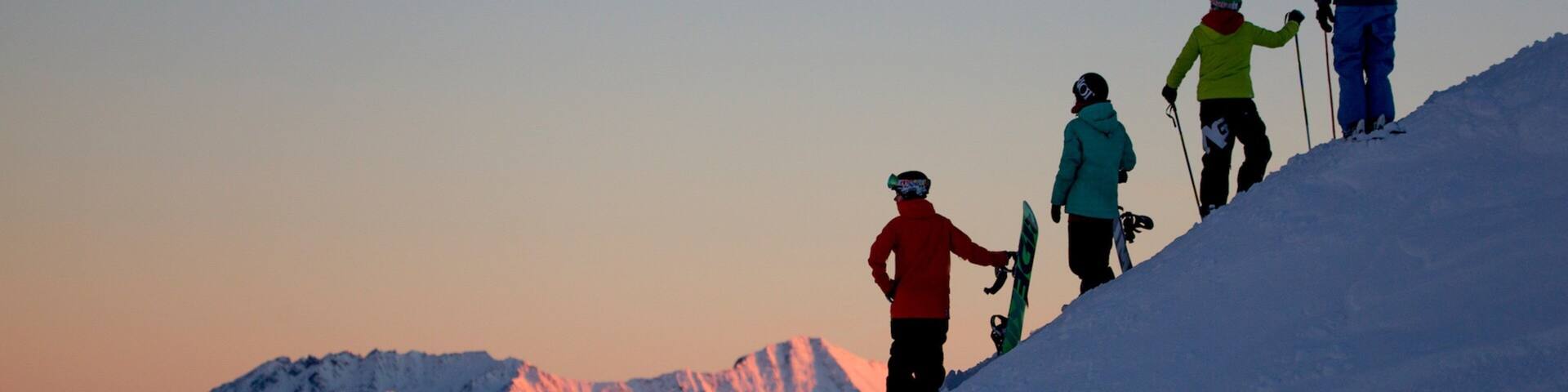 A group of skiers ascending a snowy mountain slope during sunset.