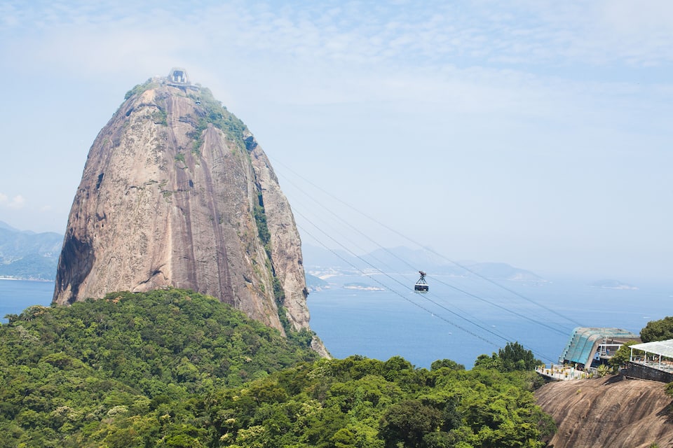 Un sistema de telefèric, una gran formació rocosa i una vista costanera.