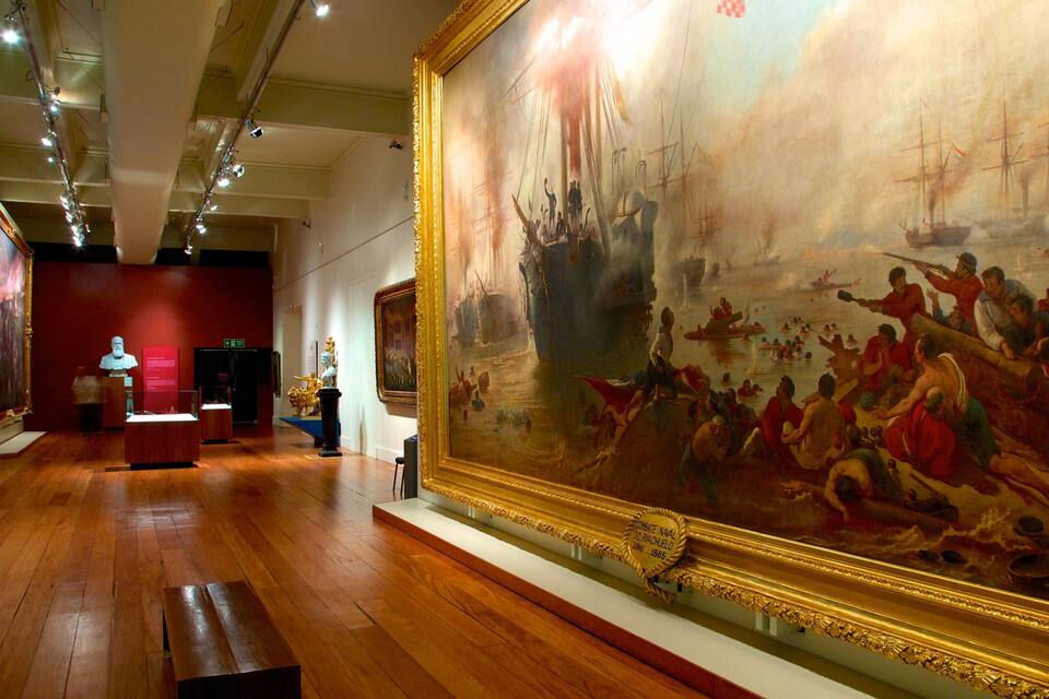 Interior de museo con un cuadro marino grande, suelos de madera y una estatua.