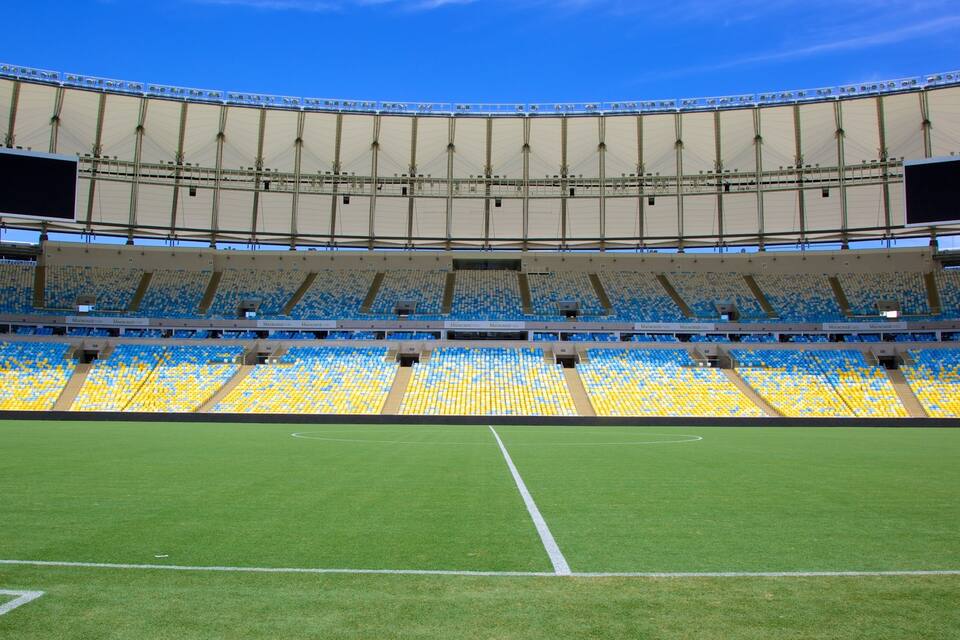 A large stadium with blue and yellow seats, a green field, and a clear blue sky.