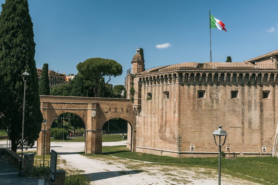 Un muro de piedra histórico con arcos, una bandera y un farol.
