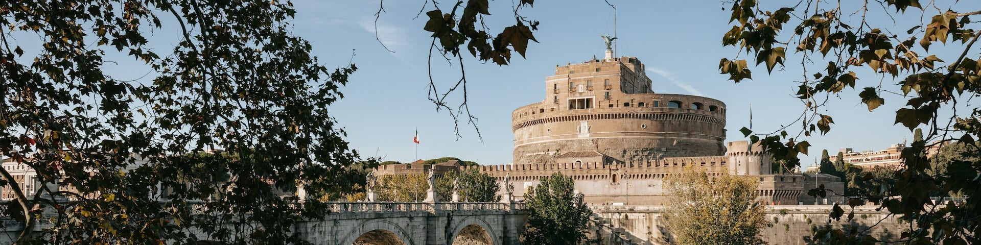 A historic building with a round tower, a stone bridge, and a river.