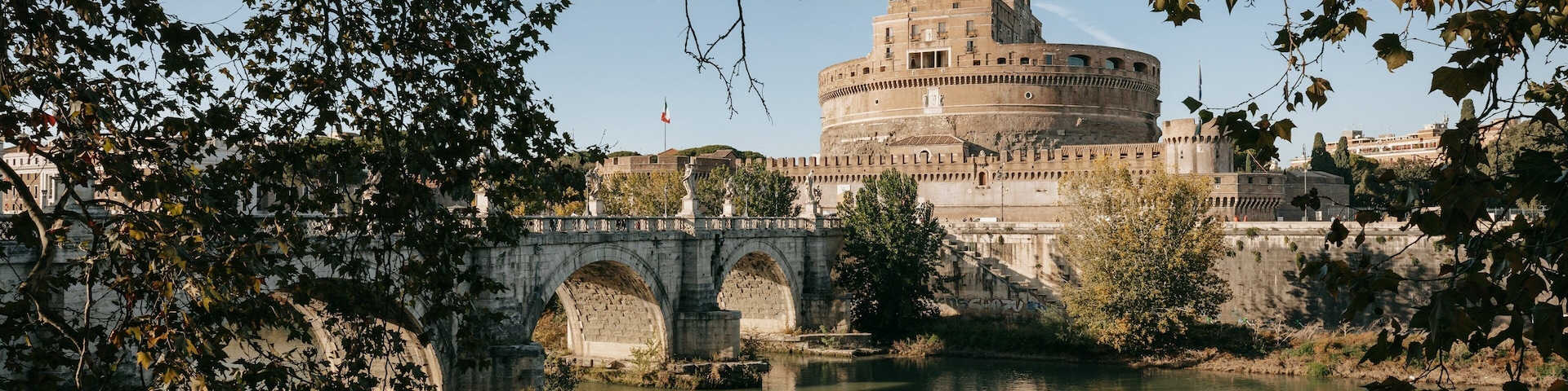 Un edificio histórico con una torre redonda, un puente de piedra y un río.