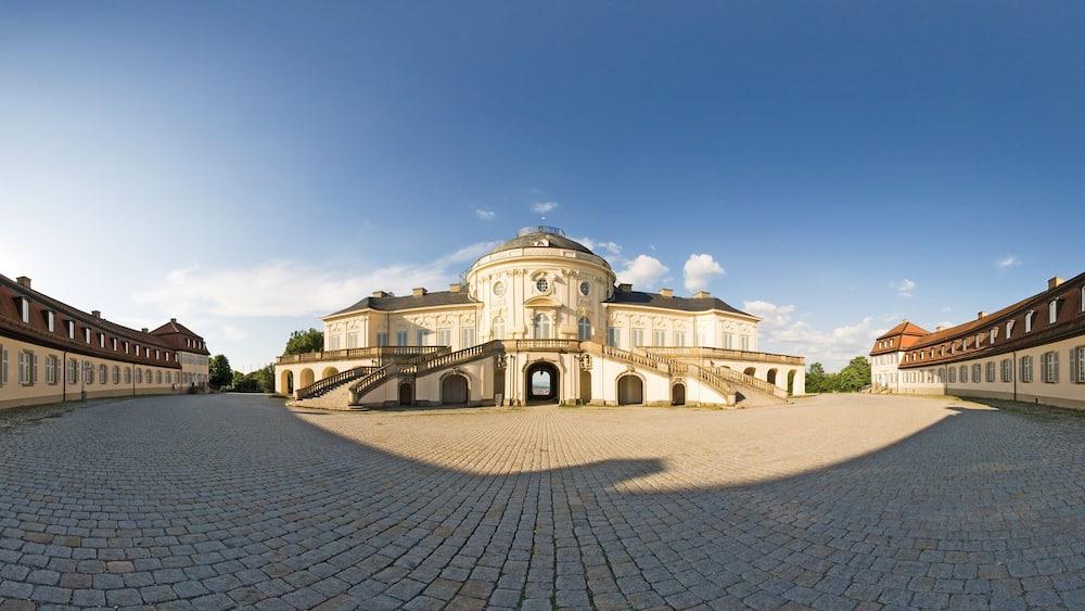 A historic building with a dome and symmetrical architecture, surrounded by a cobblestone courtyard.