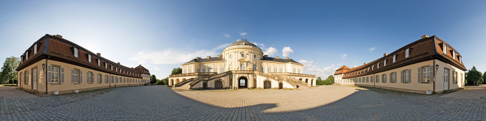A historic building with a dome and symmetrical architecture, surrounded by a cobblestone courtyard.