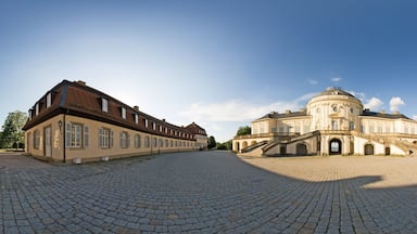 Um edifício histórico com cúpula e arquitetura simétrica, rodeado por um pátio de paralelepípedos.
