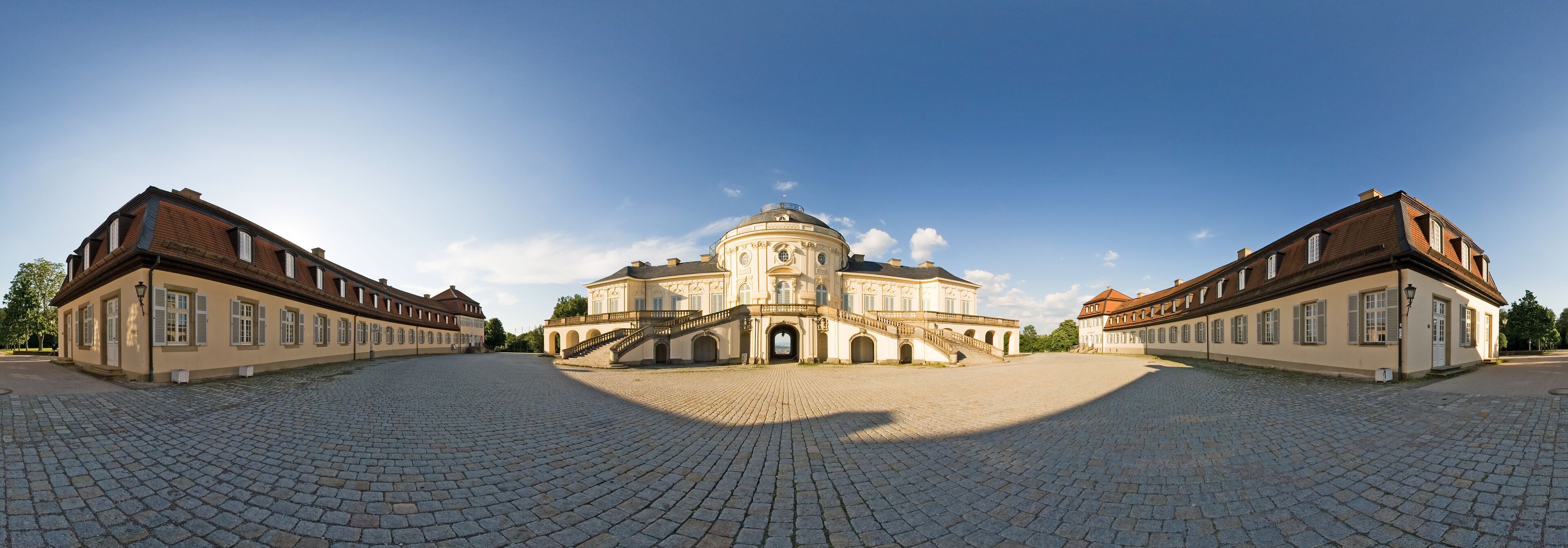A historic building with a dome and symmetrical architecture, surrounded by a cobblestone courtyard.
