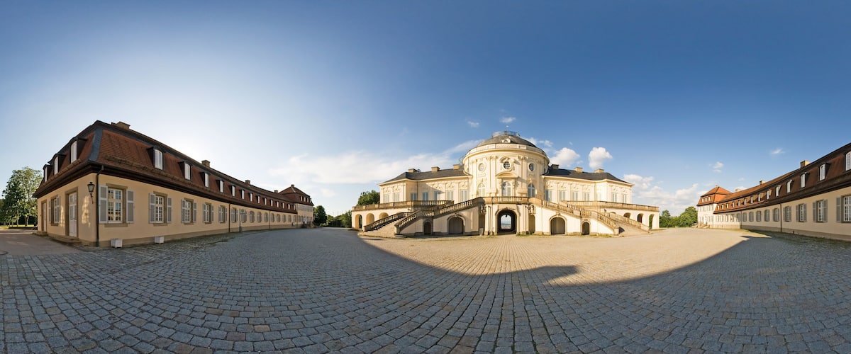 A historic building with a dome and symmetrical architecture, surrounded by a cobblestone courtyard.