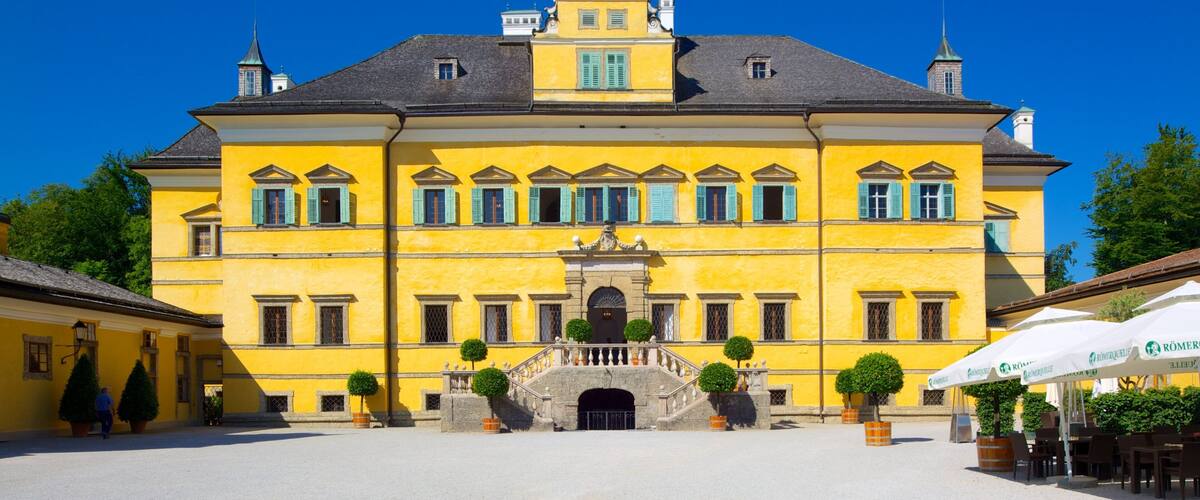 A large yellow building with a central entrance, surrounded by a courtyard with potted plants and outdoor seating.