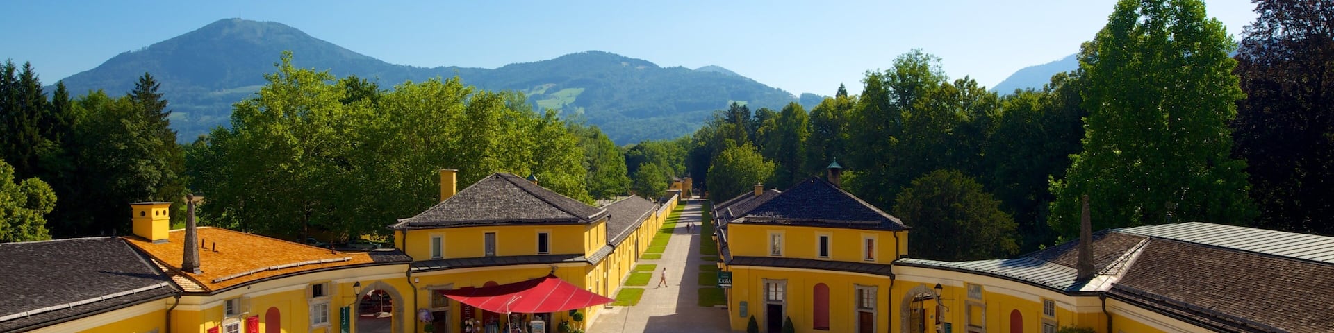 A courtyard with yellow buildings, outdoor seating, and mountains in the background.