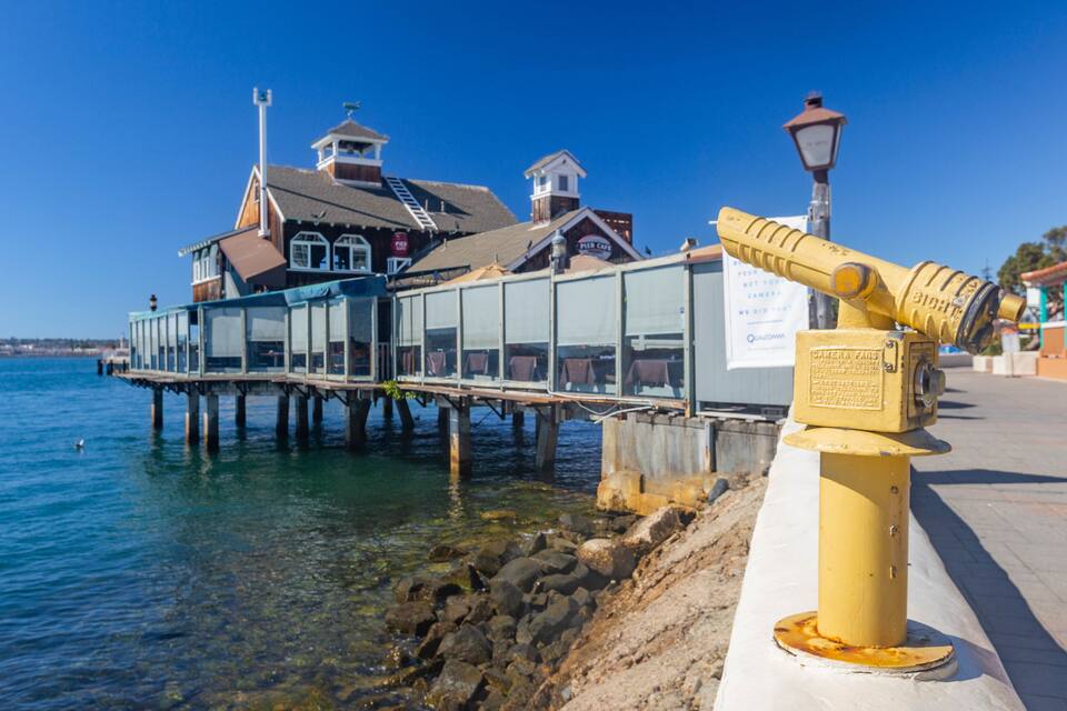 Eine Pier, die sich ins Wasser erstreckt, mit einem gelben Hydranten und einem Pier-Café im Hintergrund.