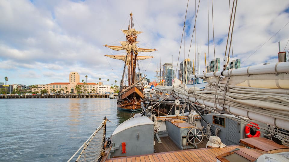 A historic sailing ship docked at a marina with a city skyline in the background.