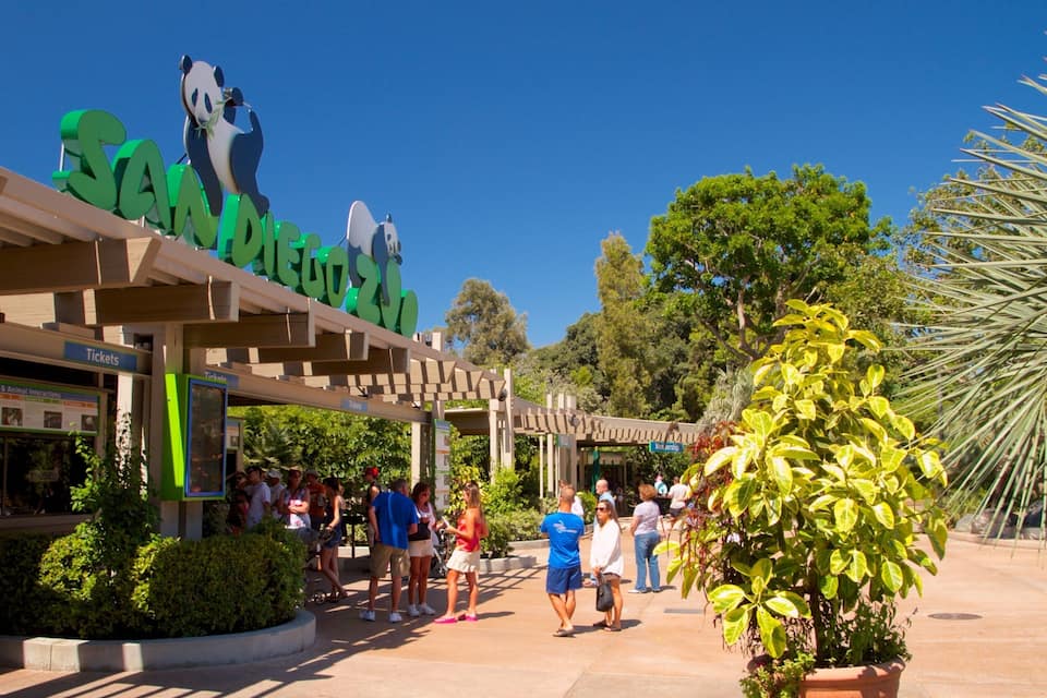 Entrada de un zoológico con una escultura de panda, taquilla y gente.
