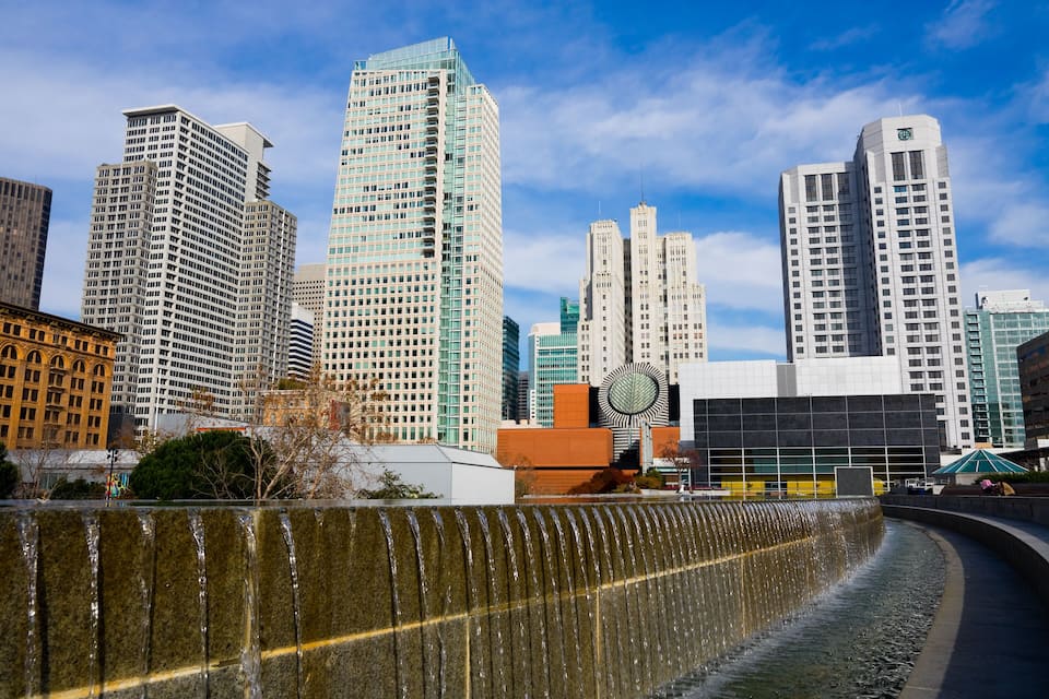 Paisagem urbana com edifícios altos, uma fonte e um edifício moderno com design circular.